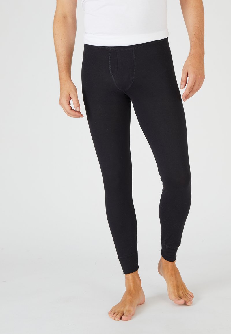 Leggings de algodón negro con un diseño ajustado, que presentan una cintura elástica y puños en los tobillos, exhibidos en un modelo descalzo.