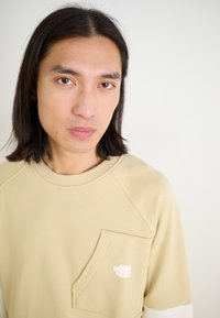 Felpa beige con superficie testurizzata, maniche raglan e taschino sul petto con logo bianco. Tessuto morbido, scollatura rotonda.