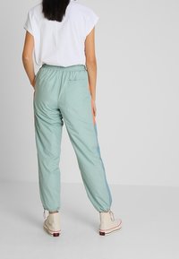 Ljust gröna sportiga joggers med elastisk midja, avsmalnande muddar, sidopaneler i blått och orange, bärs med vita högklackade sneakers och en vit topp.