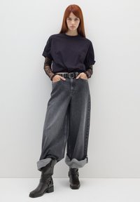 Camiseta negra de gran tamaño con mangas enrolladas, combinada con unos jeans de tiro alto y corte holgado en color gris oscuro y botas de tobillo marrones con detalle de correa.