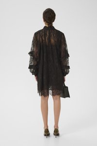 Μαύρο φόρεμα από δαντέλα με φουσκωτά μανίκια, διάφανο σχέδιο και ωοειδές στρίφωμα. Συνδυασμένο με μια μικρή πράσινη τσάντα χειρός και ελαιόχρωμα τακούνια.