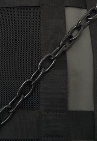 Svart veske med mesh-stoff, glatt nylonpanel og en solid svart kjedeaccent. Teksturerte stropper og kontrasterende materialer er synlige.