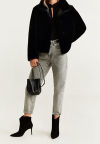 Veste en fausse fourrure noire, coupe ajustée, fermeture par boutons ; associée à un jean gris taille haute et des bottines noires à bout pointu. Petit sac à main noir.