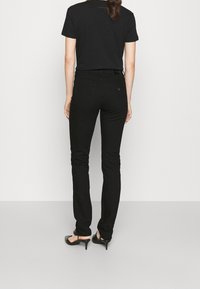 Svarta slim-fit jeans i denim, med två bakfickor och en diskret logodetalj. Kombinerat med en svart t-shirt och klackar.