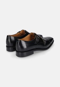 Zwarte leren schoenen met een glanzende afwerking, voorzien van een ronde neus en twee gespsieraden aan de zijkant. Lage, stevige zwarte hak.