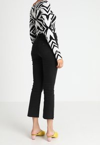 Svarta högmidjade jeans med rå nederkant, kombinerade med en svartvit zigzag-mönstrad stickad topp och gula slip-on-mules med rosa klackar.