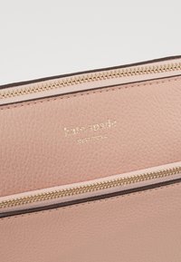 Růžová kožená peněženka se zlatým zipem, s texturovaným povrchem a raženým logem "kate spade new york".
