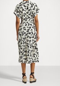 Květinové midi šaty v krémové barvě s černými okvětními lístky, krátké rukávy, zúžený pas a splývavý střih, doplněné černými klínovými botami.