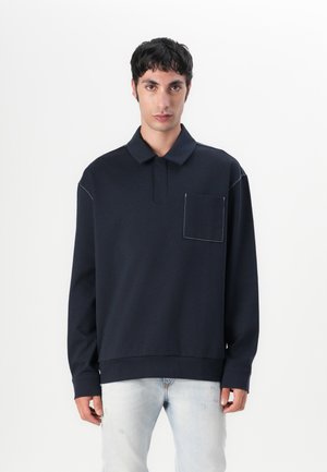 Marineblauwe longsleeve polo met een kraag, voorzien van een borstzak en contrasterende stikdetails. De stof ziet er zacht en soepel uit.