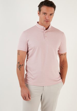 Camisa polo rosa hecha de tela suave, con cuello y tres botones. Mangas cortas y un diseño ajustado con una textura suave.