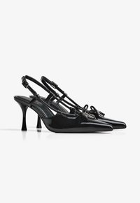 Fekete lakkbőr pántos magas sarkú cipő hegyes orral, vékony pántokkal és állítható csatokkal. 3 hüvelykes tűsarkúval rendelkezik.