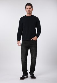 Μαύρο φούτερ με στρογγυλή λαιμόκοψη από βαμβάκι, συνδυασμένο με σκούρο τζιν με ξεβαμμένη υφή. Υποδήματα: μαύρα αθλητικά παπούτσια με λευκές ρίγες.