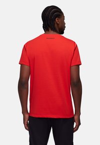 Rotes Baumwoll-T-Shirt mit kurzen Ärmeln, verfügt über einen Rundhalsausschnitt und ein kleines schwarzes Logo auf dem Rücken. Glatte Textur, lässiger Sitz.