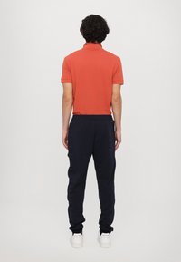 Rød polo shirt med krave, parret med marineblå sweatpants. Bukserne har en afslappet pasform med elastiske manchetter og hvide sneakers.