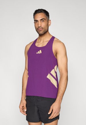 Lühikeste tume juustega mees, kes kannab lilla varrukateta sportlikku särk ja musti lühikesi pükse, näoga otse vaataja poole heleda ühevärvilise tausta ees.