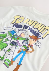 Chemise blanche avec les personnages de Toy Story Rex, Buzz l'Éclair et Woody, et un grand texte jaune indiquant "To Infinity and Beyond!"