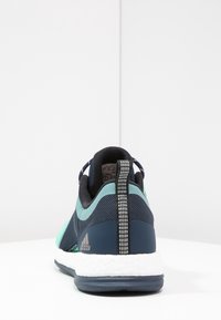 Scarpa da ginnastica blu navy e teal con tomaia in mesh, dettagli testurizzati e linguetta riflettente sul tallone. Intersuola in schiuma bianca per ammortizzazione.