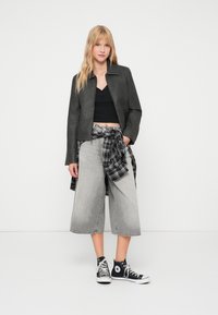 Veste en cuir synthétique gris avec un design à col, associée à un crop top noir et un large culotte en denim gris, le tout terminé par des baskets montantes noires.
