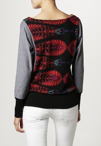 Pull noir et gris avec un dos à motifs présentant des designs floraux rouges et verts. Manches longues, style ajusté et texture de tissu douce.