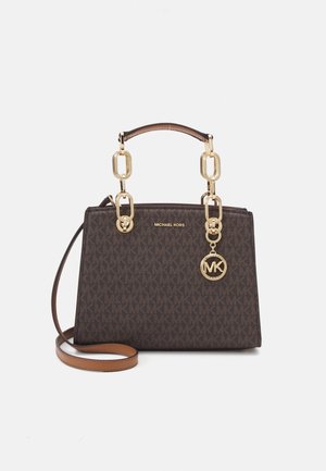 Bruine Michael Kors handtas met gouden kettinghandvatten, logohanger en afneembare schouderband tegen een effen lichte achtergrond.