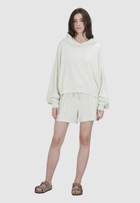 Jasnozielona bluza z kapturem z oversize'owymi rękawami w zestawie z dopasowanymi szortami. Miękka tekstura, elastyczny pas na sznurki i swobodny design.