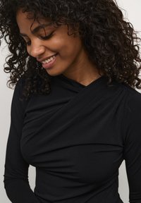 Haut noir à manches longues avec un design drapé et un tissu texturé, comportant des détails froncés aux épaules et une silhouette ajustée.