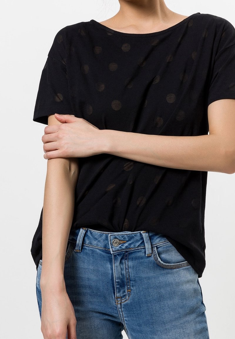Camiseta negra de corte holgado con un sutil patrón de lunares y mangas cortas, combinada con vaqueros de denim de color azul claro.