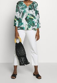 Wzorzysta bluzka z motywem zielonych i białych liści, o luźnym kroju. Połączona z białymi, krótkimi jeansami, czarną plecioną torebką i czarnymi sandałami na płaskim obcasie.
