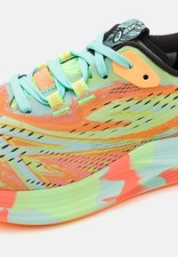 Zapatilla de running Asics con un diseño de colores brillantes, cordones turquesa, ojal naranja y suela multicolor en tonos verde, naranja y azul.