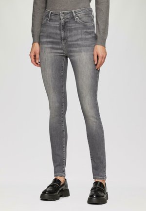 Enges Jeans in einem verblichenen Grauwaschung, mit hoher Taille, glatter Denim-Oberfläche und klassischem fünftaschen Design. Kombiniert mit glänzenden schwarzen Mokassins.