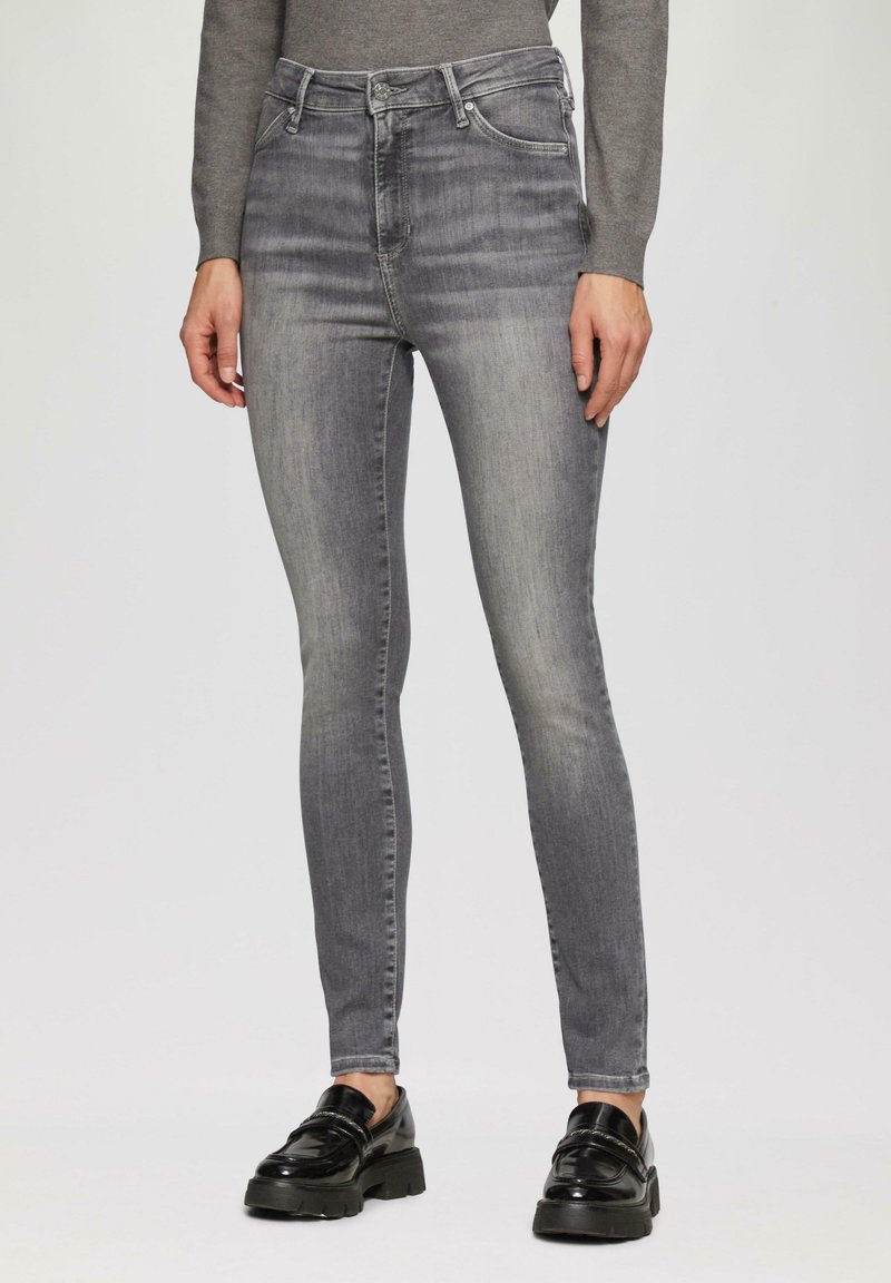 Jean skinny en délavé gris, avec une taille haute, une texture en denim lisse et un design classique à cinq poches. Associé à des mocassins noirs brillants.