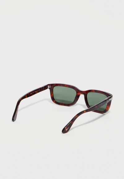 Ορθογώνια γυαλιά ηλίου με σχέδιο χελώνας και σκούρους πράσινους φακούς, με ελαφρώς κυρτά πλαϊνά, ανοιγμένα και τοποθετημένα πάνω σε ανοιχτόχρωμη επιφάνεια.