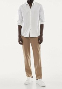 Weißes Hemd mit Knopfleiste, beiger Hose und weißen Sneakers. Verfügt über einen klassischen Kragen und hochgekrempelte Ärmel. Glatte Stoffstruktur.