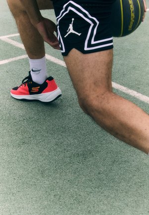 Fekete testű kosárlabda cipők, rózsaszín részletekkel és fehér talppal. Fehér zoknival és logóval ellátott fekete sorttal viselve.