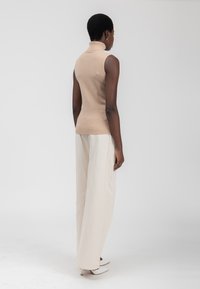 Top color crema senza maniche con design aderente. Abbinato a pantaloni larghi di un beige chiaro e tacchi bianchi appuntiti.