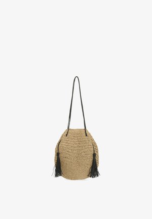 Bolso de hombro tejido beige con largas correas negras y borlas negras decorativas en cada lado.