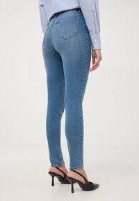 Cienkie niebieskie dżinsy z wysokim stanem, z tylnymi kieszeniami i subtelnym przetarciem. Połączone z czarnymi mule na obcasie.