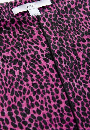 Elastiska leggings i ett rosa tyg med ett mönster av svart leopardprickar, med en vikbar midja och synlig sömdetalj.