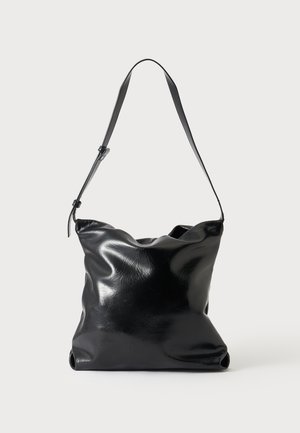 Sac à épaule en cuir noir brillant avec une seule bandoulière réglable et une forme rectangulaire souple et décontractée sur un fond uni.