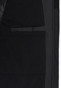 Veste en polaire noire avec une doublure intérieure lisse, une poche à rabat et des détails de couture contrastés le long des bords.
