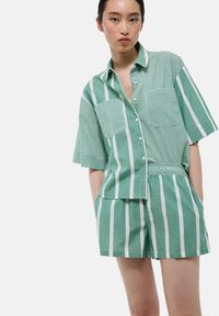 Chemise à manches courtes rayée vert et blanche avec deux poches poitrine et un short assorti. Tissu doux et coupe décontractée.