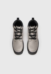 Par de botas de senderismo gris claro con suelas negras, cuellos acolchados y cordones negros, vistas desde arriba sobre un fondo blanco.