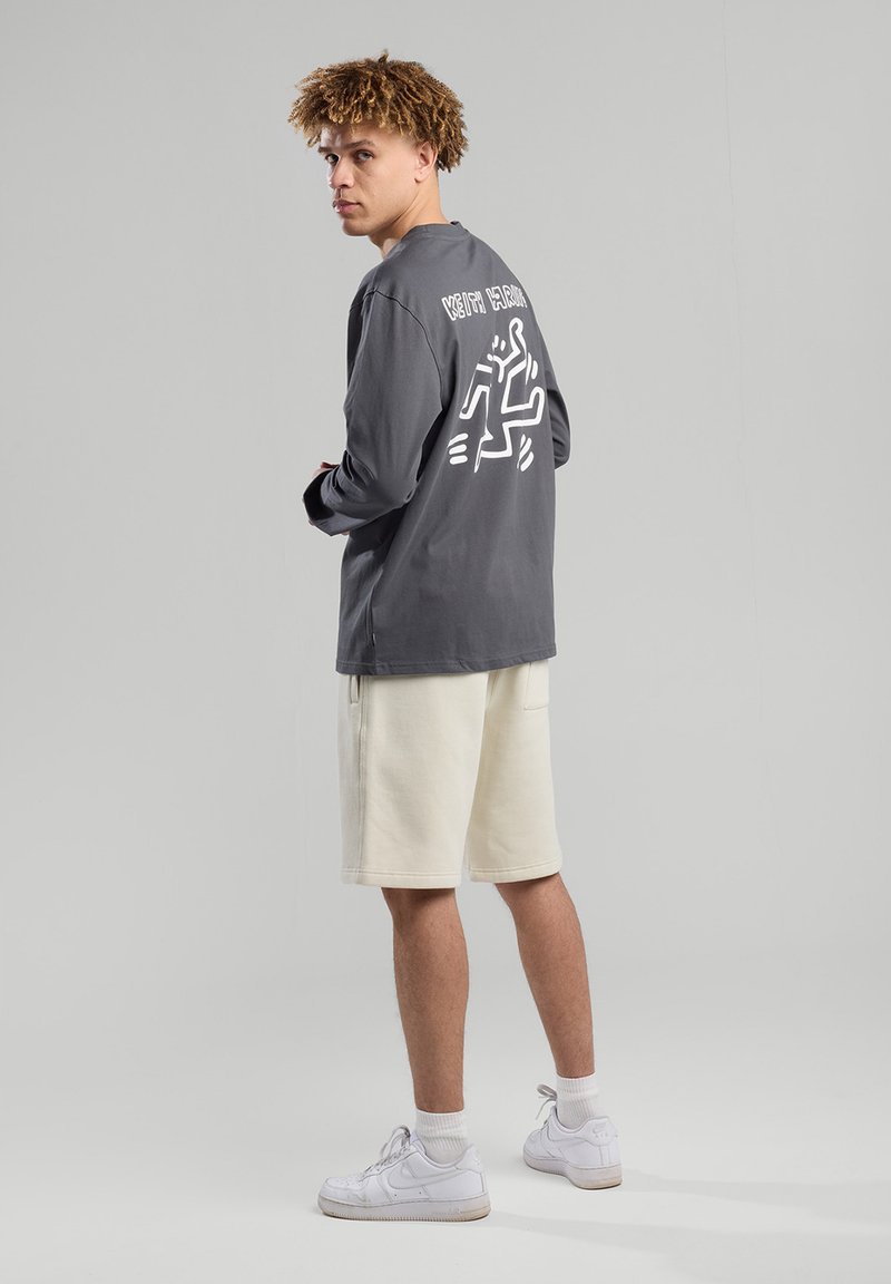 Long-sleeve gray shirt with white graphic on back, paired with cream shorts and white sneakers. Smooth fabric, relaxed fit, casual design.