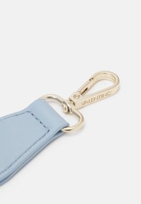 Ljusblå lädernyckelring med ett metallspänne i guldfärg, med synliga sömmar och varumärkesnamnet "VALENTINO" ingraverat på metallbeslaget.