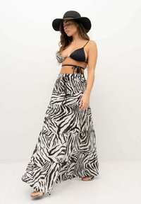 La gonna maxi presenta un design a strati con un motivo zebravero bianco e nero. Abbinata a un top bikini nero e un cappello a tesa larga.