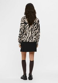 Langærmet top med zebramønster i beige og sort, parret med en sort nederdel og knæ-høje brune sokker. Sorte chunky sko fuldender looket.