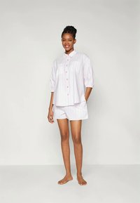 Set pidžame sa svijetloružastim prugama, koja se sastoji od košulje s dugmadima kratkih rukava i odgovarajućih kratkih hlača. Košulja ima širok kroj i pastelne gumbe.