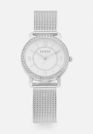 Silver mesh band watch featuring a round white face, crystal bezel, and embossed hour markers. Brand name "GUESS" visible on the dial.