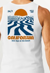 White sleeveless shirt featuring a graphic design with blue ocean waves, an orange sun, and text: "CALIFORNIA slow days at the beach."