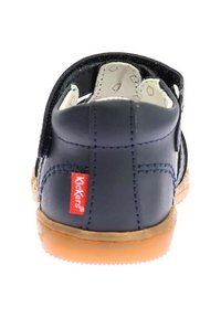 Scarpa per bambini in pelle blu navy con cinturino in velcro, suola in gomma beige e logo Kickers rosso sul tallone. L'interno presenta una fodera decorata.